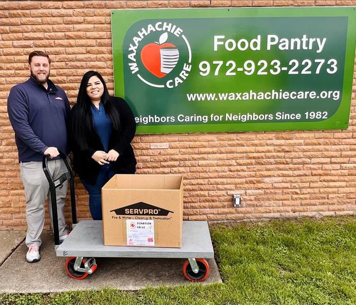 Male and female in front of wall mural with box of food donations